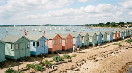 Row of pastel-painted wooden beach huts along the shingle shoreline at West Mersea, Essex, in July.